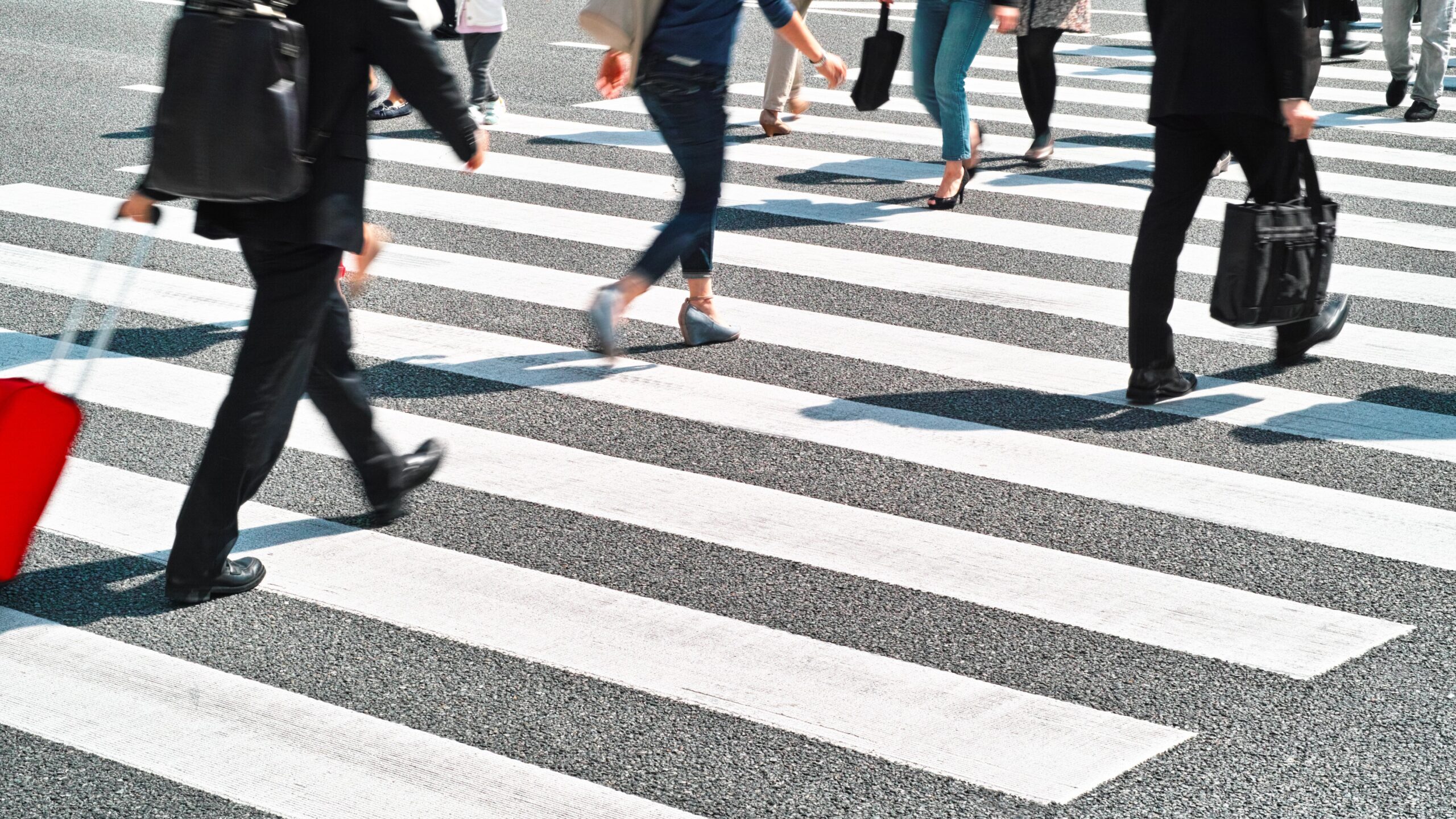 Pedestrians crossing a zebra-striped crosswalk in an urban street.