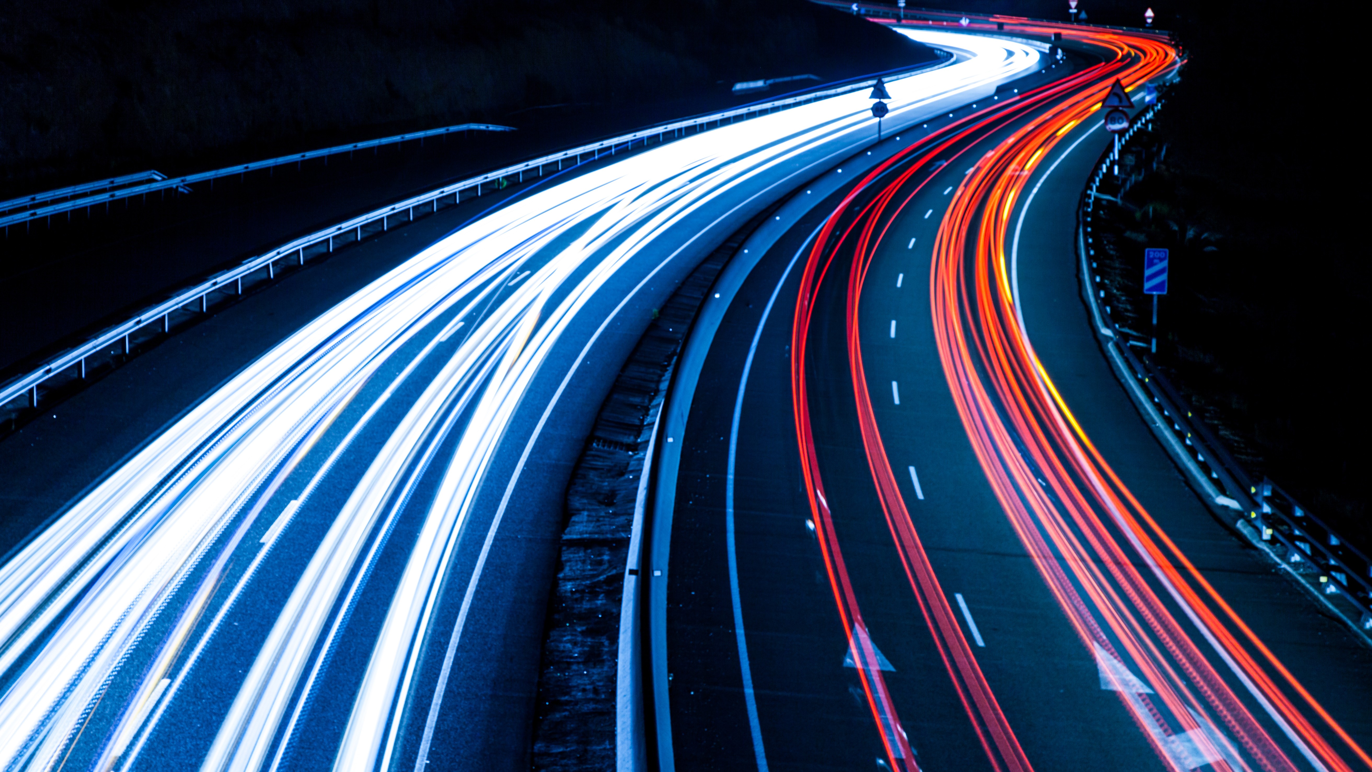 Nighttime highway with blue and red light trails curving along the road, created by long-exposure photography.
