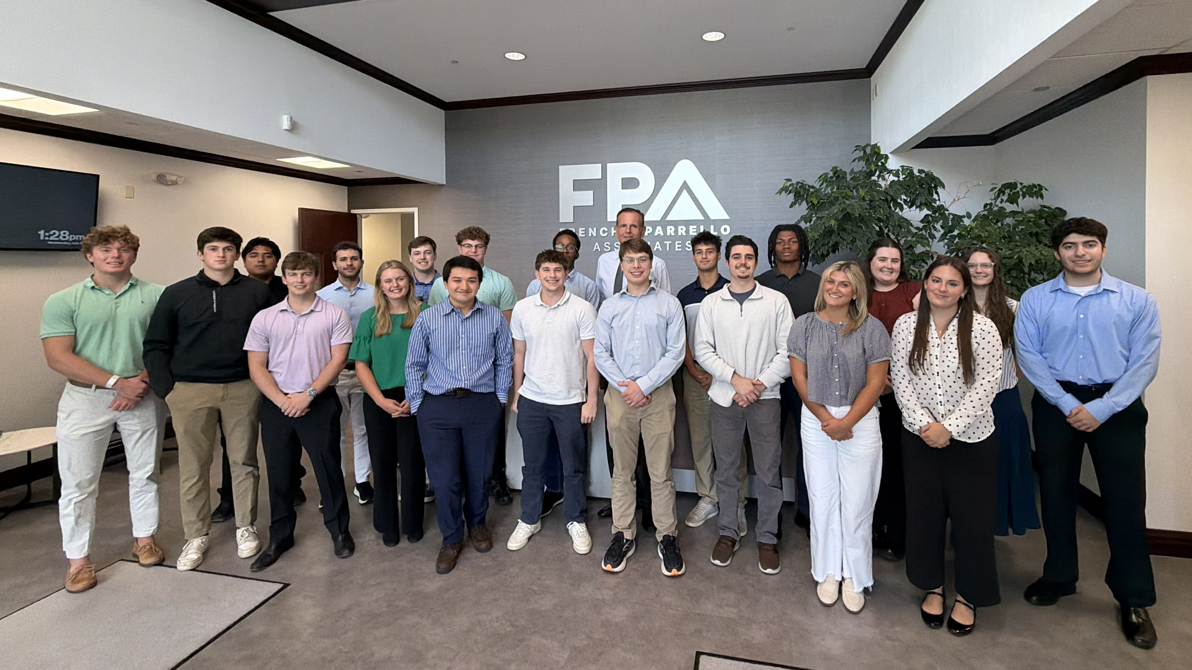 Group of about 20 young professionals posing for a photo in a modern office lobby, with a large FPA logo on the back wall behind them.