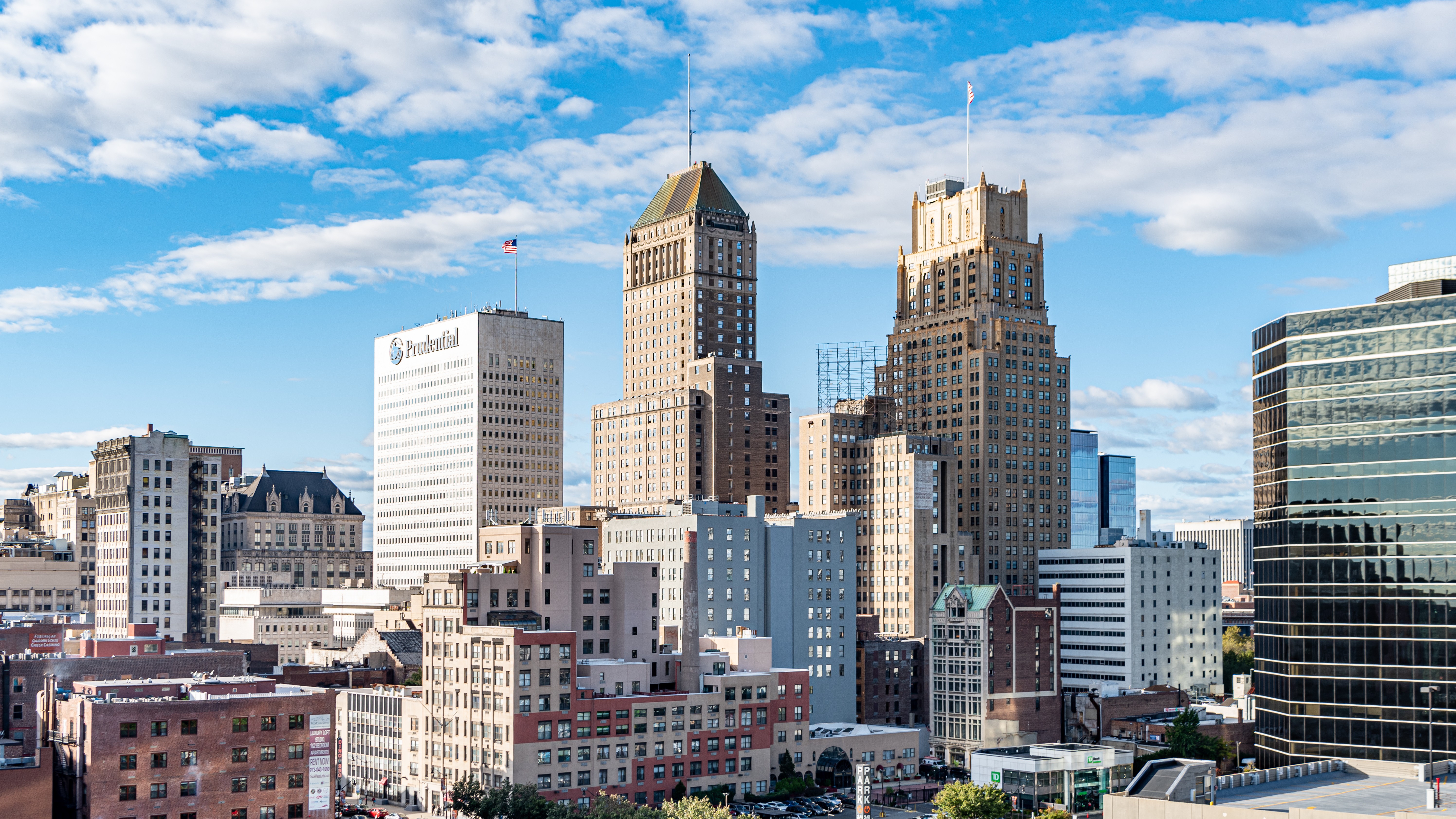 Downtown skyline with two tall brick buildings and a white office tower under a blue sky with scattered clouds, Prudential signage visible on the white building.